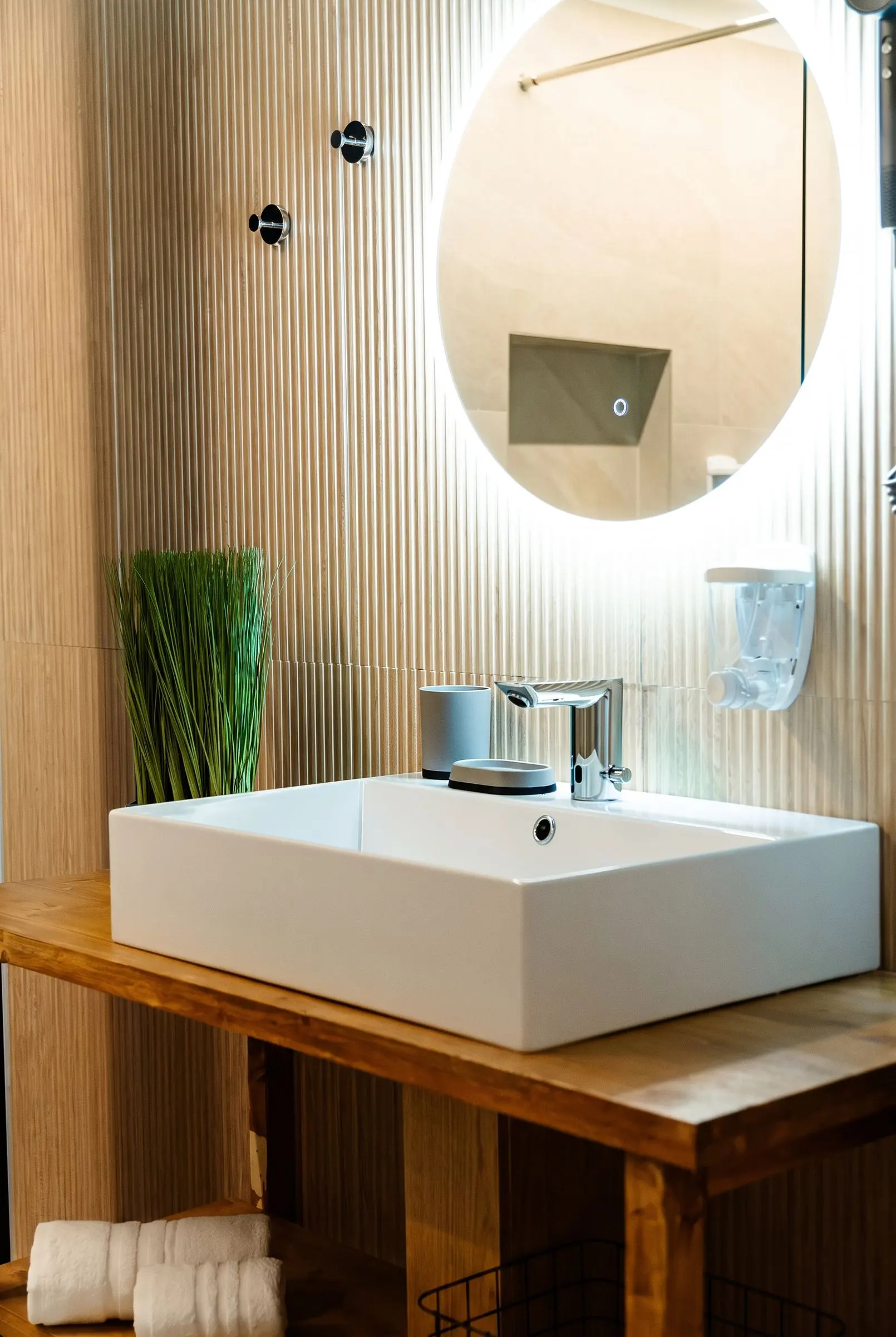 Il bagno con il lavabo squadrato sul piano in legno e lo specchio tondo retroilluminato