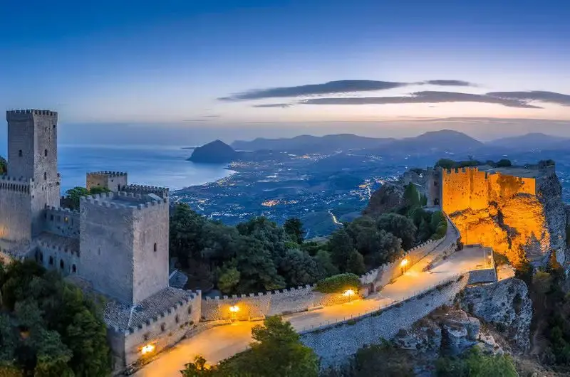 Erice all’imbrunire, il castello di Venere e le torri illuminate sopra il golfo