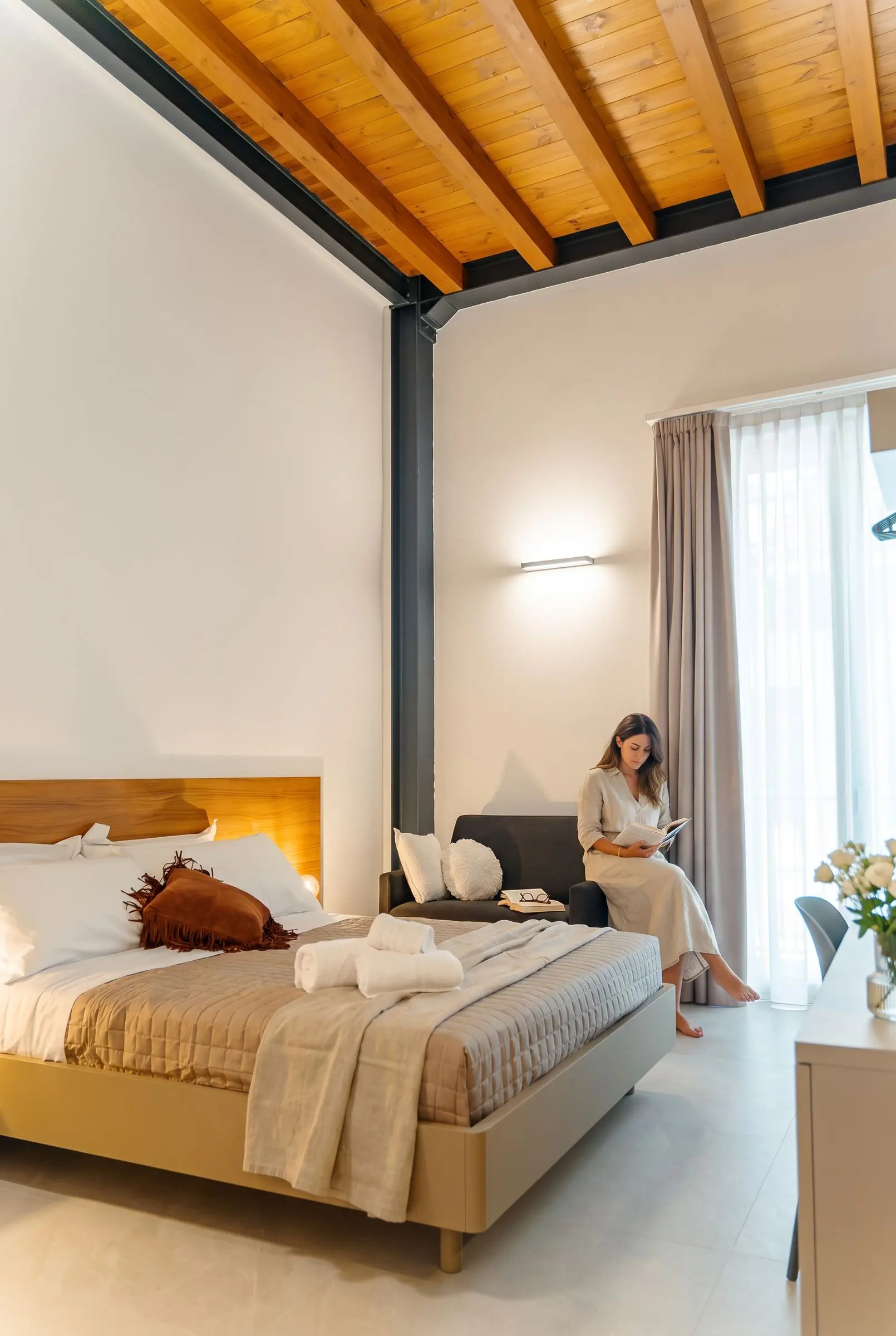 La camera Olea con il soffitto in legno, il letto e la poltrona vicino alla finestra