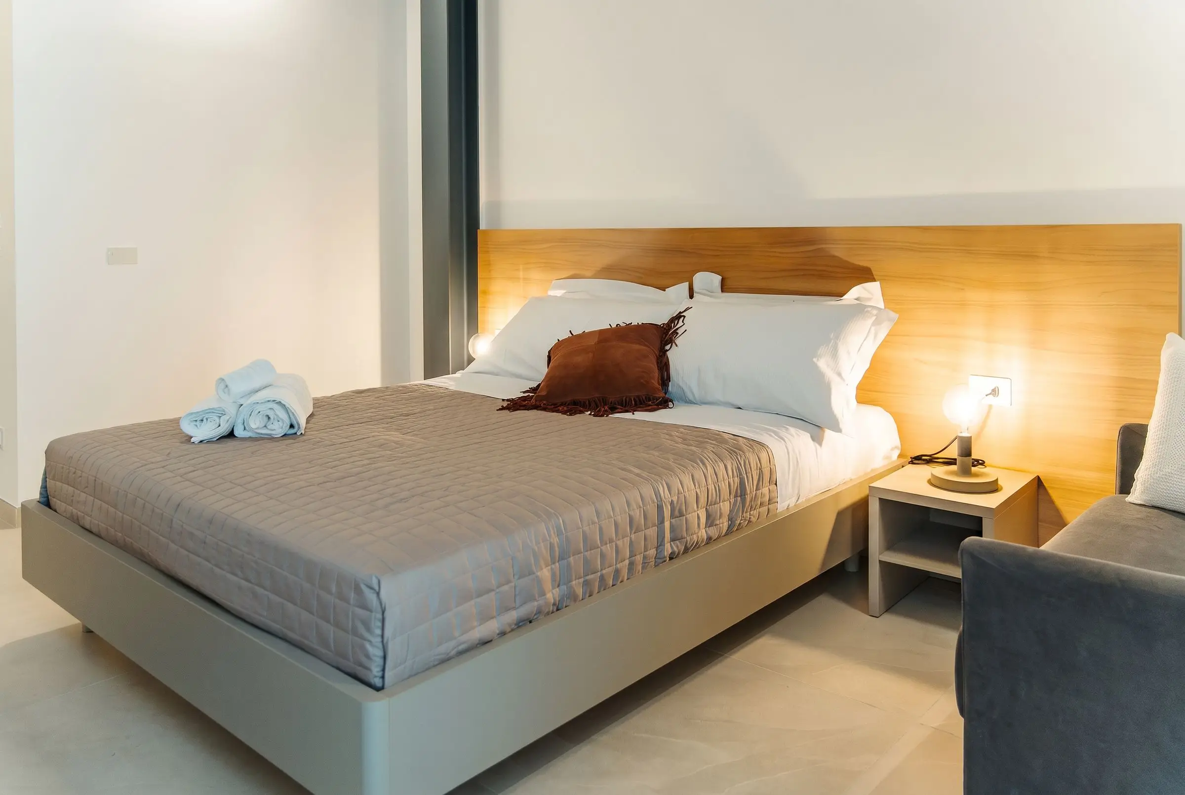 La camera Olea, il letto con la testiera in legno e la poltrona
