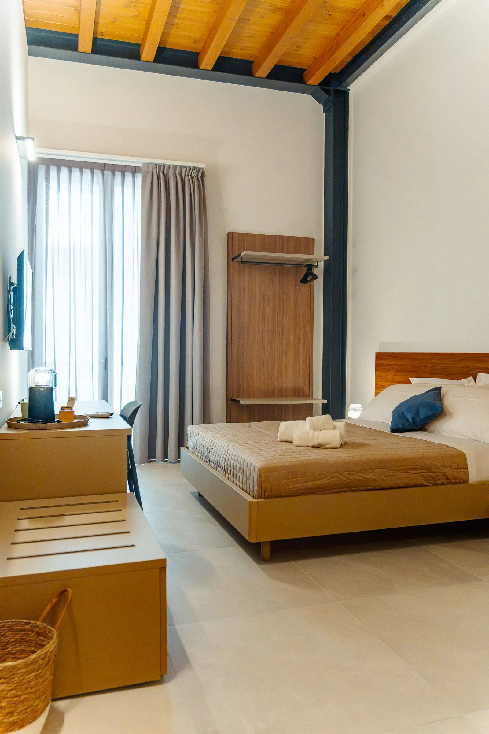 La camera Vitis dall'ingresso, le travi in legno e il letto con il copriletto senape